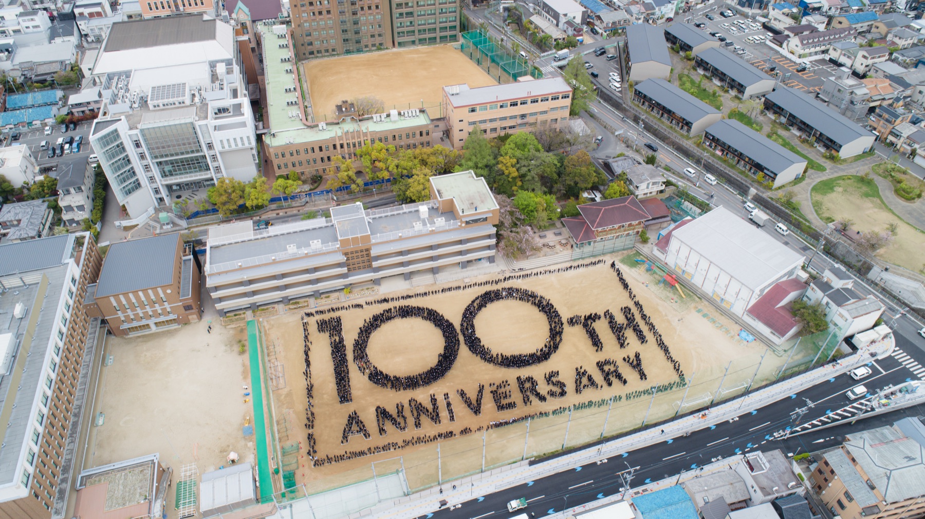 校庭に人文字で「100th ANNIVERSARY」を描いた空撮写真